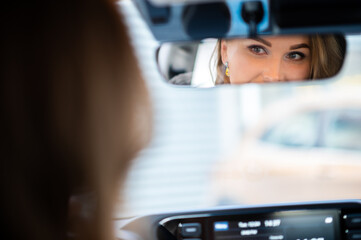 Young lady driving her car reflected in the rear view mirror