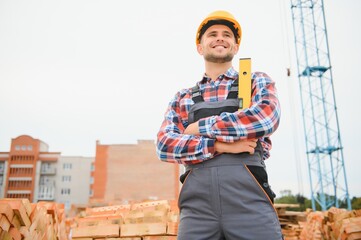 Construction worker man in work clothes and a construction helmet. Portrait of positive male builder in hardhat working at construction site.