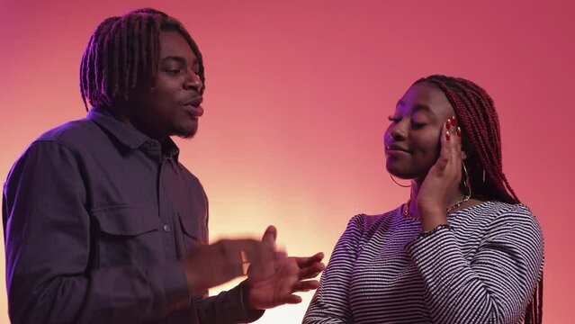 Different plans. Couple misunderstanding. Neon light portrait. Inspired black man describing his desirable things to skeptic displeased woman on purple peach pink background.