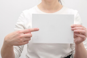 a woman holding a blank blank white sheet of paper, points with her index finger.