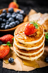 A pile of pancakes with berries and honey. 