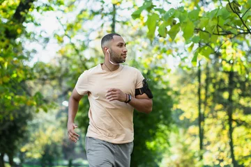 Rugzak Hispanic man jogging in the park on a sunny day, runner listening to music in wired headphones, audio books and podcasts, sportsman happy with an active weekend. © Liubomir