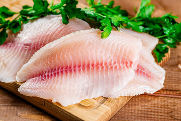 Raw fish fillet with parsley on a cutting board. 