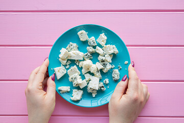 Female hands hold turquoise plate with cheese and cauliflower. Healthy snack concept. Pink wooden background. 