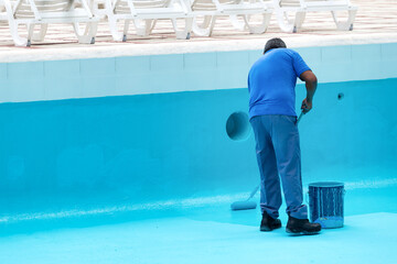 Unrecognizable worker repainting swimming pool in blue colour
