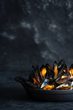 Mussels in a pan and a Glass of white wine. Black background. Food photography. Low key. Copy place.