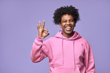 Young happy hipster African American teen guy student wearing pink hoodie isolated on purple...