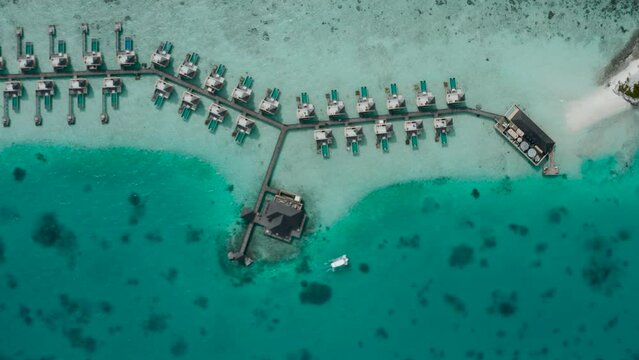 aerial overhead shot getting closer to the maldives islands showing a group of water villas over the ocean 4k