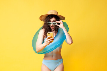 young shocked brunette girl in a blue swimsuit with a swimming inflatable ring holds a smartphone