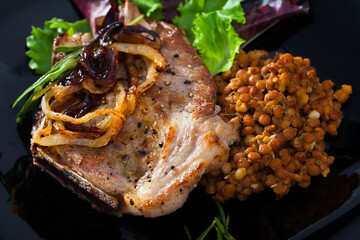 Close-up image of roasted pork chop with lentils and greens