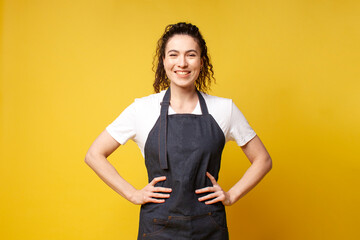 portrait of young barista girl in uniform on a yellow background, woman waiter in denim apron smiling