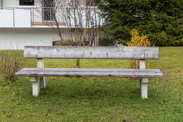 A gray wooden bench is outside in autumn