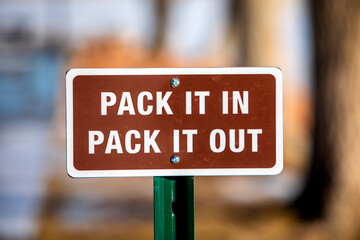 a brown, pack it in, pack it out sign with white lettering and white boarder