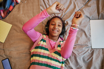 Top view black teenage girl listening to music laying on bed