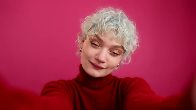 Portrait of caucasian, blonde-haired woman looking at camera with isolated pink background behind. Portrait of a smiling girl looking stylish and glamorous. High quality 4k footage