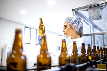 Female factory supervisor controlling beer production in alcohol beverage bottling plant.
