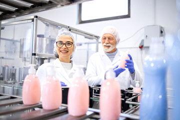 Happy smiling factory workers producing shampoo and liquid soap for cleaning industry.