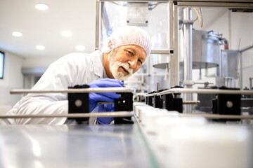 Production line worker standing by conveyor machine and controlling manufacturing of cosmetics products.