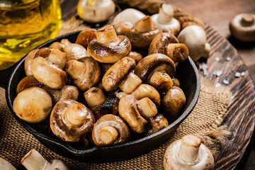 Frying pan with fried mushrooms on a wooden tray. 