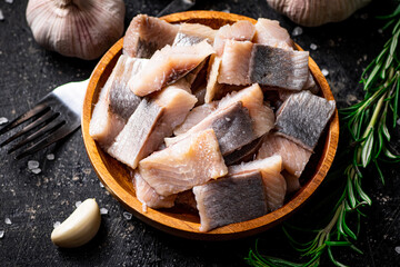 Salted herring on a wooden plate with garlic and rosemary. 