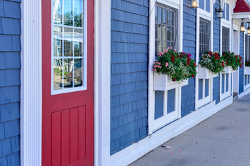 The exterior entrance to a shop with a bright red door and glass window. There are three windows in...