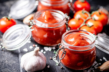 Tomato sauce in glass jars on a stone board with spices. 