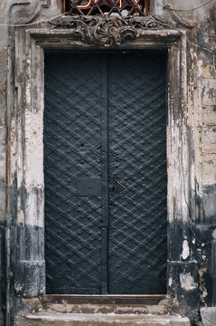 Doorway with old matte wrought iron black metal door with stripes and rivets in Lviv, Ukraine. Vintage background with peeling paint close up.
