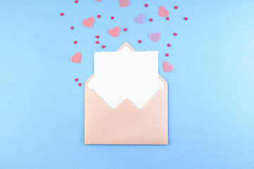 Pink envelope with blank white paper card inside and Valentine hearts on pastel blue background....