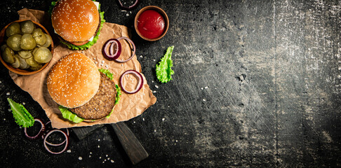 Fototapeta na wymiar Burger on a cutting board with onion rings, tomato sauce and lettuce. 