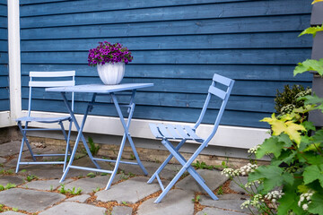 A purple colored metal patio table near a blue wooden horizontal clapboard siding exterior wall....