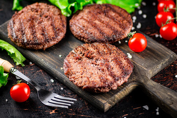 Burger grill on a cutting board with tomatoes and greens. 
