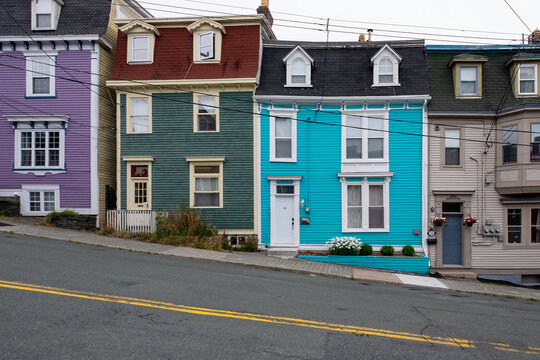 St. John's, NL, Canada - January 2023: A row of multiple colorful wooden vintage row houses painted bright cheerful colours. There's a paved street with yellow lines in front of the neighborhood. 