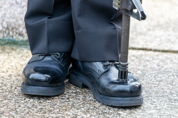 A  military person stands at attention with his rifle pitched on the toe of his shinned boot. The male navy officer stands on guard wearing dark pants, black boots, and a rifle resting on the uniform.