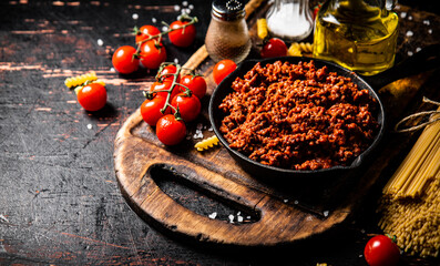 Bolognese sauce on a cutting board with cherry tomatoes and dry pasta. 