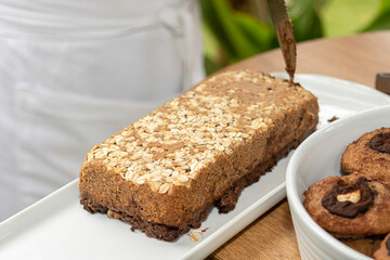delicioso bolo caseiro de banana com aveia muito saudável numa travessa branca pronta para servir e ao fundo o avental da cozinheira desfocado
