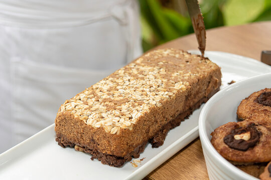 delicioso bolo caseiro de banana com aveia muito saud&aacute;vel numa travessa branca pronta para servir e ao fundo o avental da cozinheira desfocado