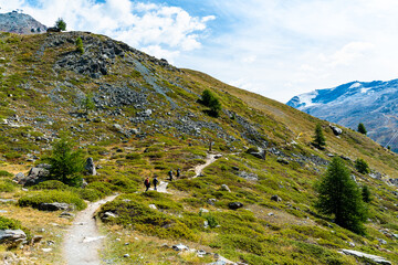 Tourists hiking on The Five Lakes Trail in Zermatt with the majestic natural landscape in the background.