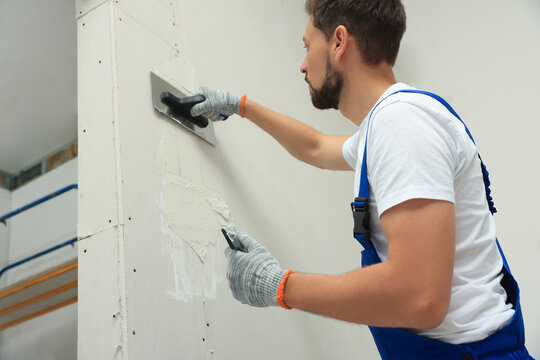 Professional worker plastering wall with putty knives indoors
