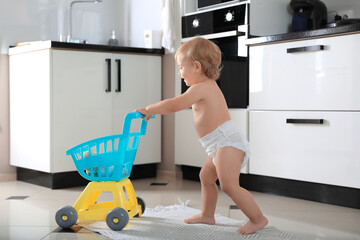 Cute baby with toy walker in kitchen. Learning to walk