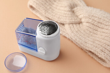 Modern fabric shaver with fuzz and knitted headdress on pale orange background, closeup. Space for...