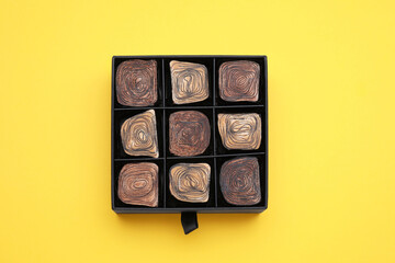 Box of tasty chocolate candies on yellow background, top view