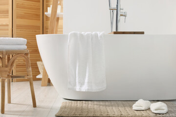 Stylish tub, wicker stool, slippers and soft towels in bathroom
