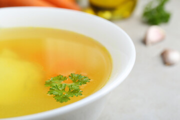 Delicious chicken bouillon with parsley on light grey textured table, closeup