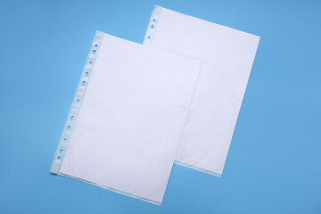 Punched pockets with paper sheets on light blue background, flat lay. Space for text