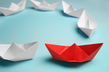 Group of paper boats following red one on light background. Leadership concept