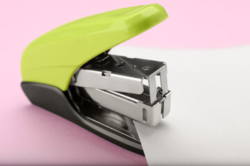 New bright stapler with paper sheet on pink background, closeup