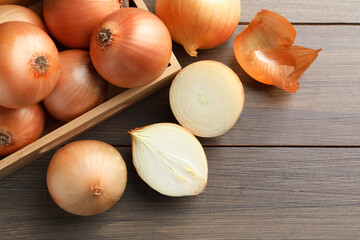 Whole and cut onions on wooden table, flat lay