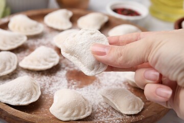 Woman holding raw dumpling (varenyk) with tasty filling at wooden board, closeup