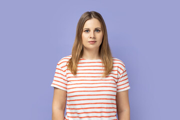 Obraz premium Portrait of serious confident blond woman wearing striped T-shirt standing looking at camera with attentive look, being strict and bossy. Indoor studio shot isolated on purple background.