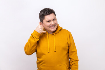 Portrait of handsome cheerful man holding telephone hand gesture near ear, imitating communication on phone, wearing urban style hoodie. Indoor studio shot isolated on white background.